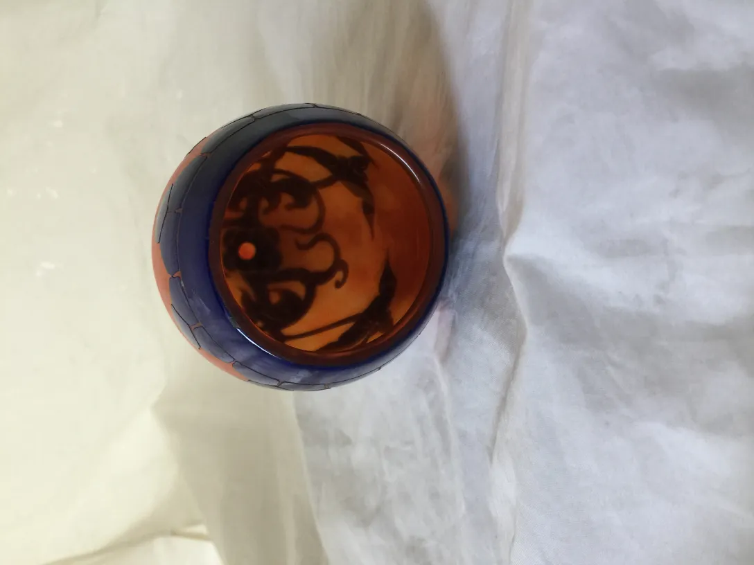 Vidro assinado Le Verre com detalhes intrincados e cores quentes em fundo claro.