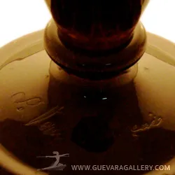 Vidrio firmado Le Verre con detalles decorativos en fondo claro.