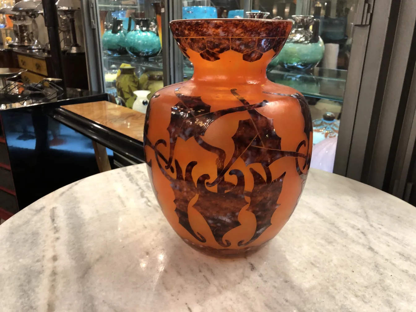 Glass vase with signed details, featuring orange and brown accents, placed among antique displays.