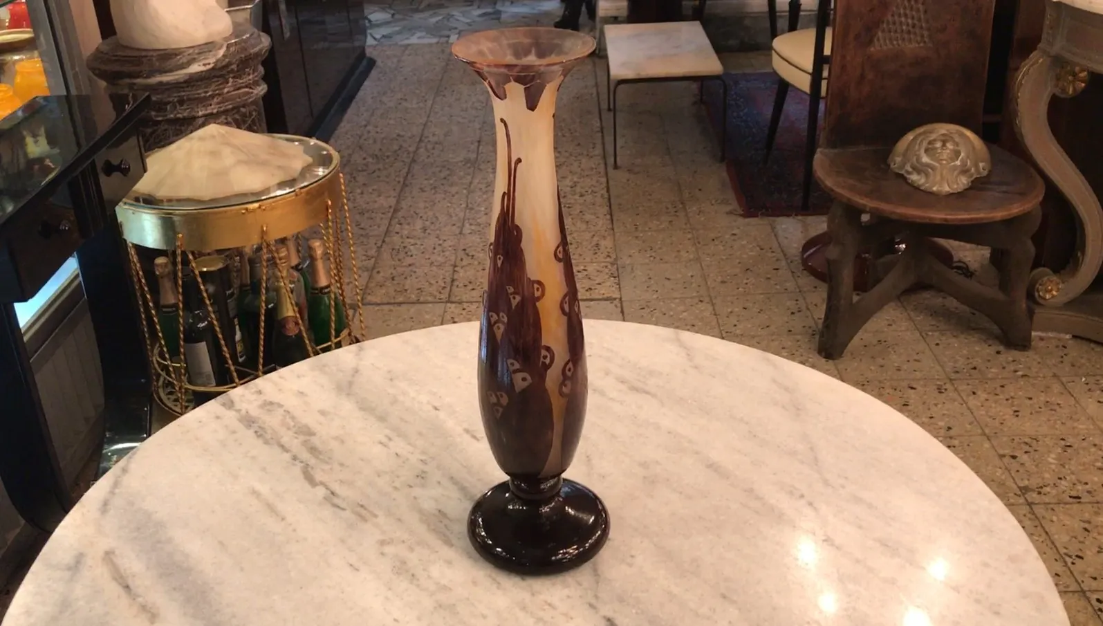 Высокая ваза подписанного стекла Le Verre с декоративными деталями в коричневых тонах и элегантным дизайном, расположенная на мраморном столе.