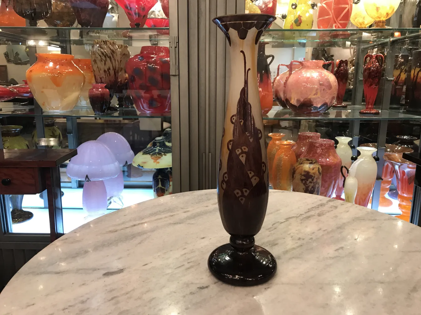 Vaso con design ornato, sfondo chiaro, su uno scaffale con altri oggetti decorativi