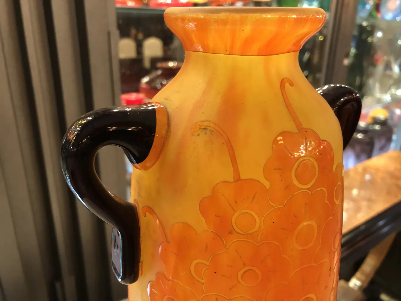 Jarra antiga de vidro assinado Le Verre com decorações florais em tons quentes, destacando-se em um ambiente de coleção.