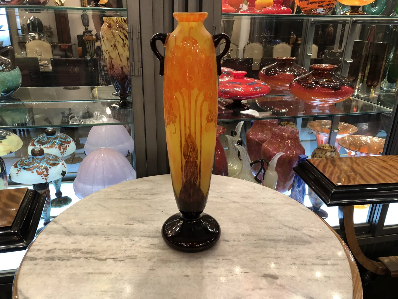 Antiguo vaso de vidrio firmado Le Verre, con colorido diseño art nouveau, en un ambiente de antigüedades.