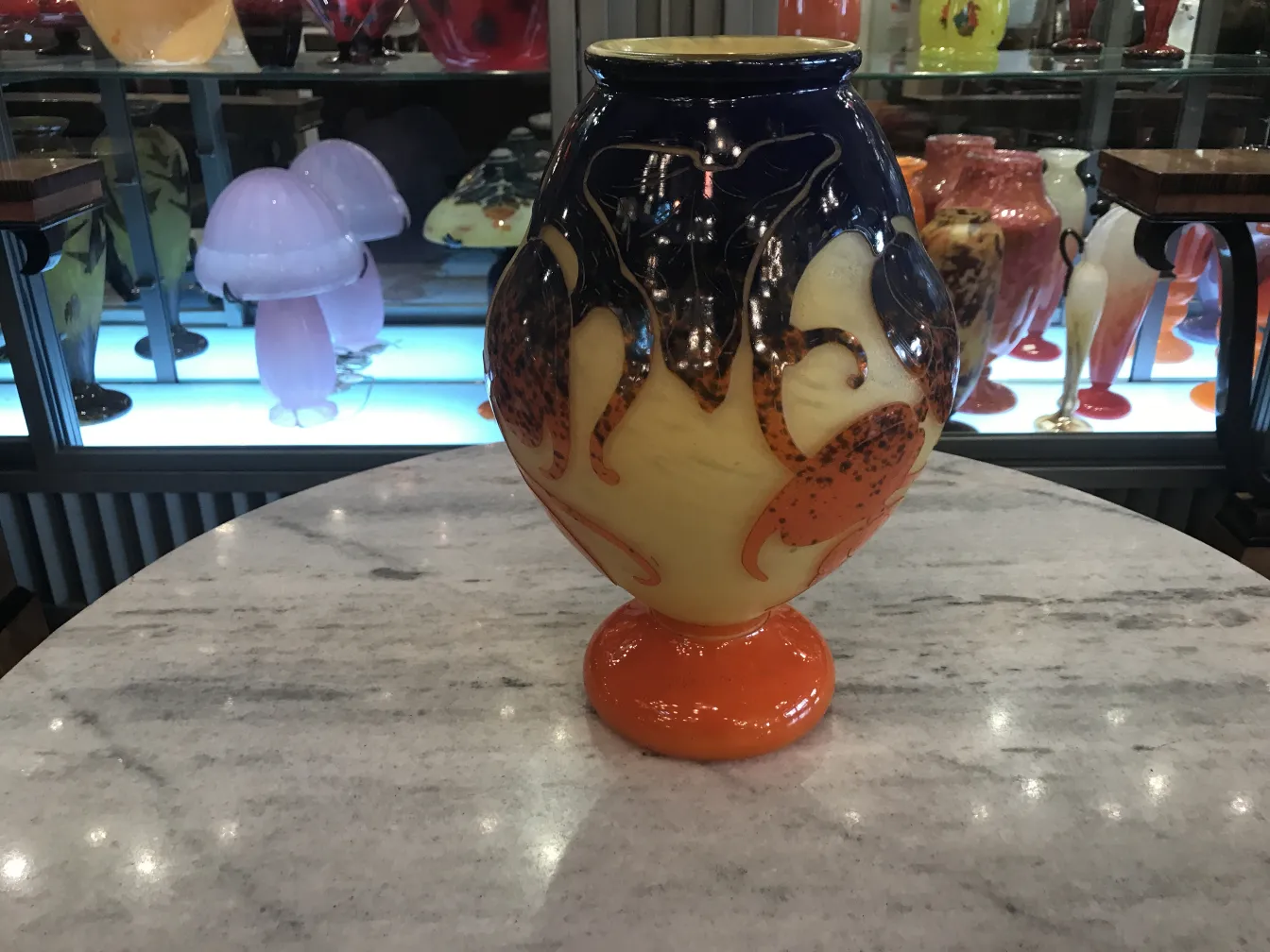 Vaso antico in vetro firmato con dettagli arancioni e blu, sfondo espositivo.