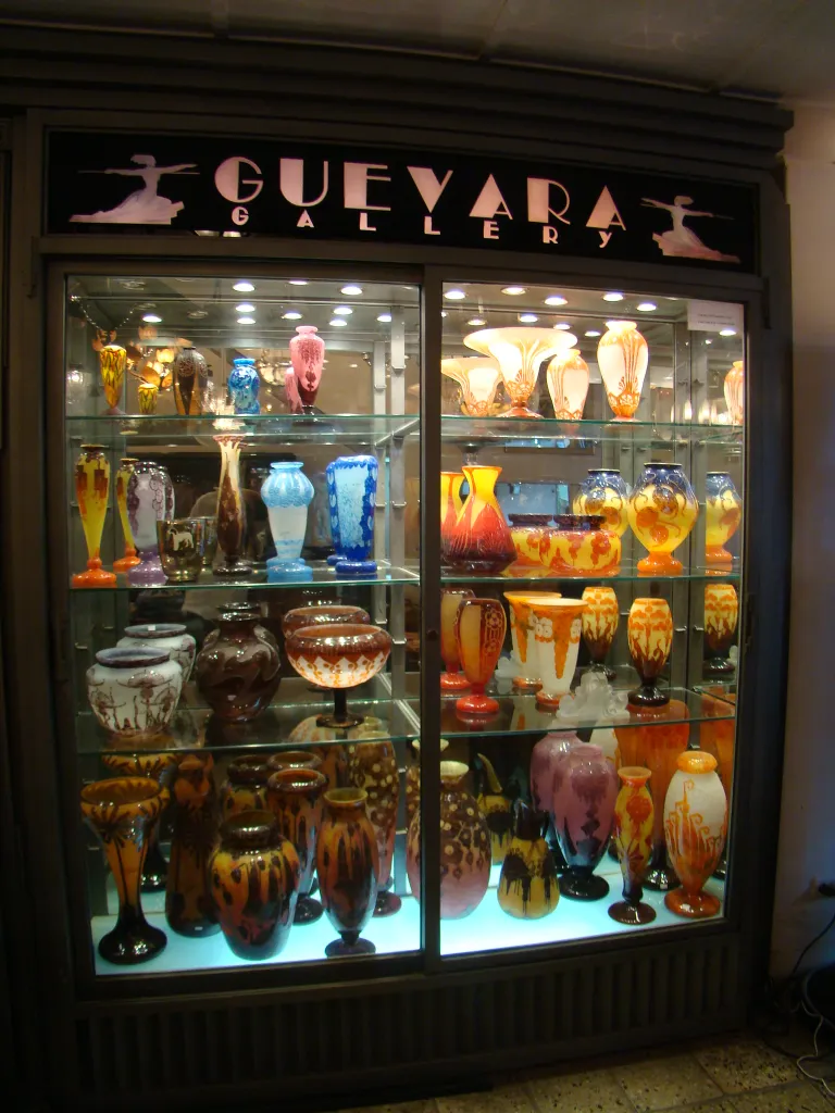 Vitrine exibindo antiguidades de vidro assinado Le Verre francês em várias formas e cores.