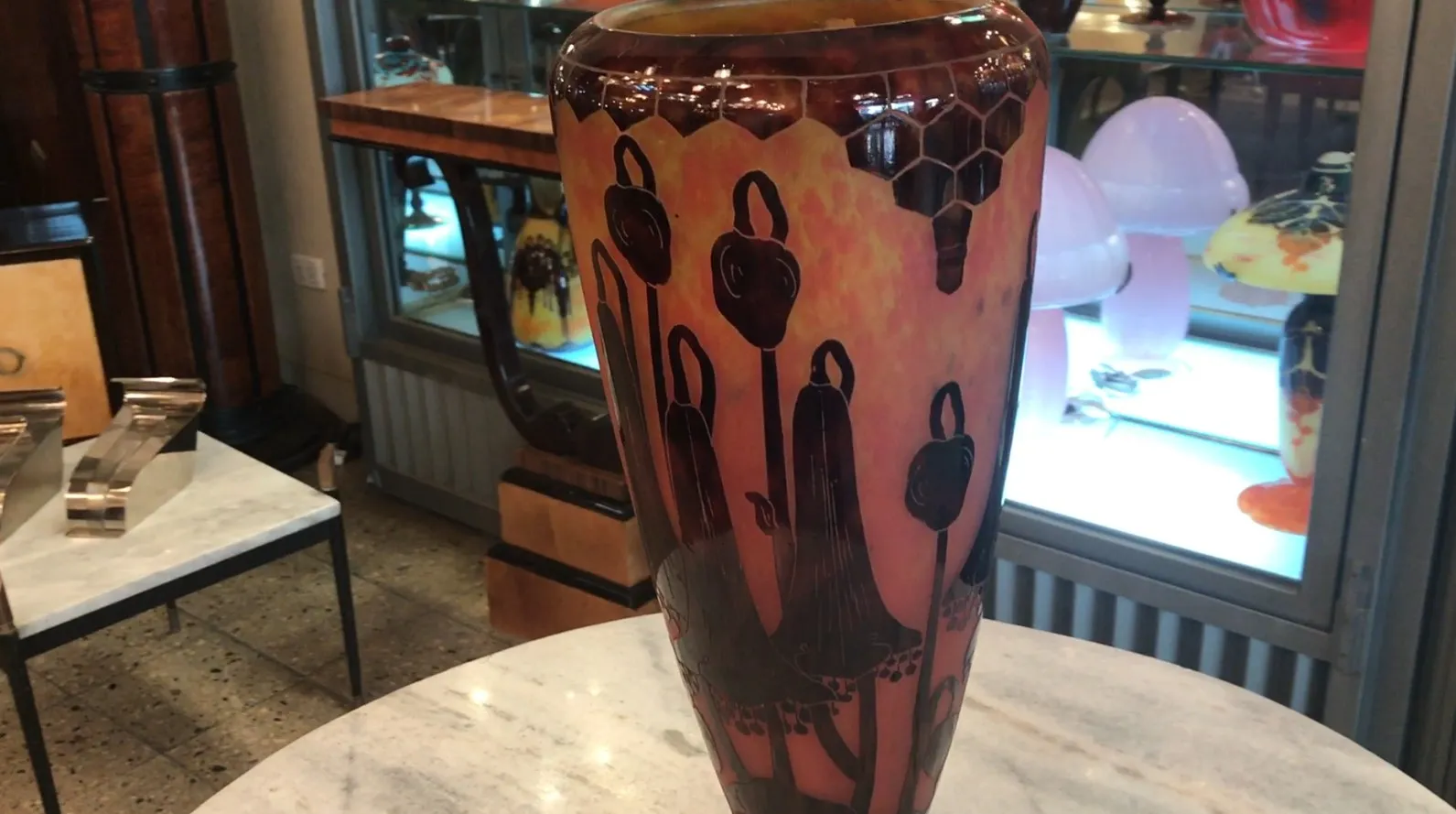 Vaso de vidro assinado Le Verre com cores quentes, exposto em ambiente de antiguidades.