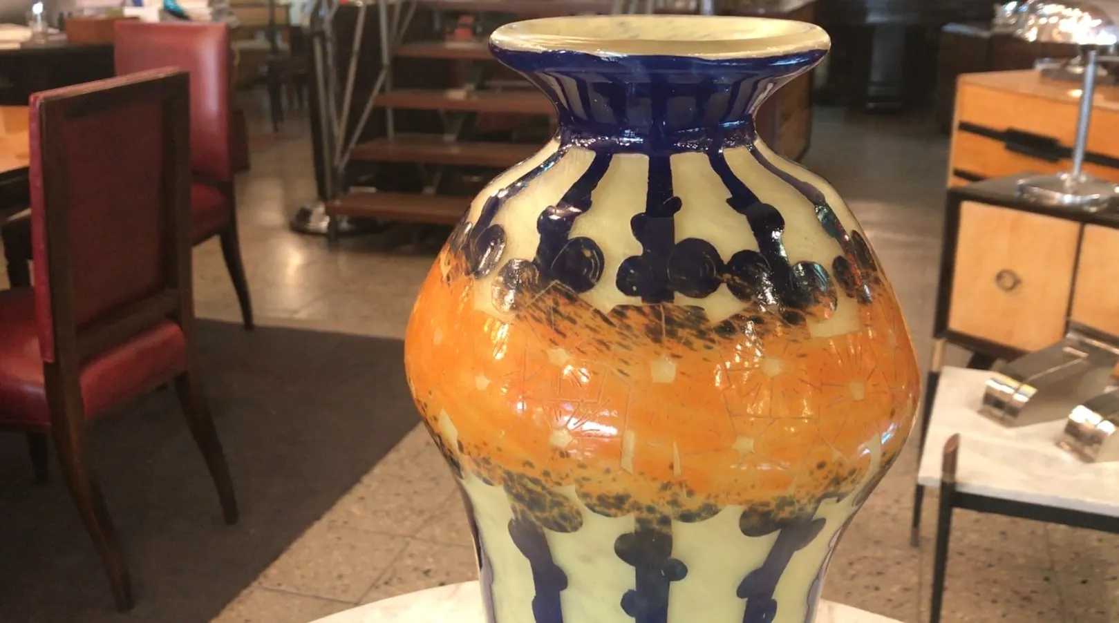 vase en verre signé avec des motifs orange et bleu parmi des meubles anciens