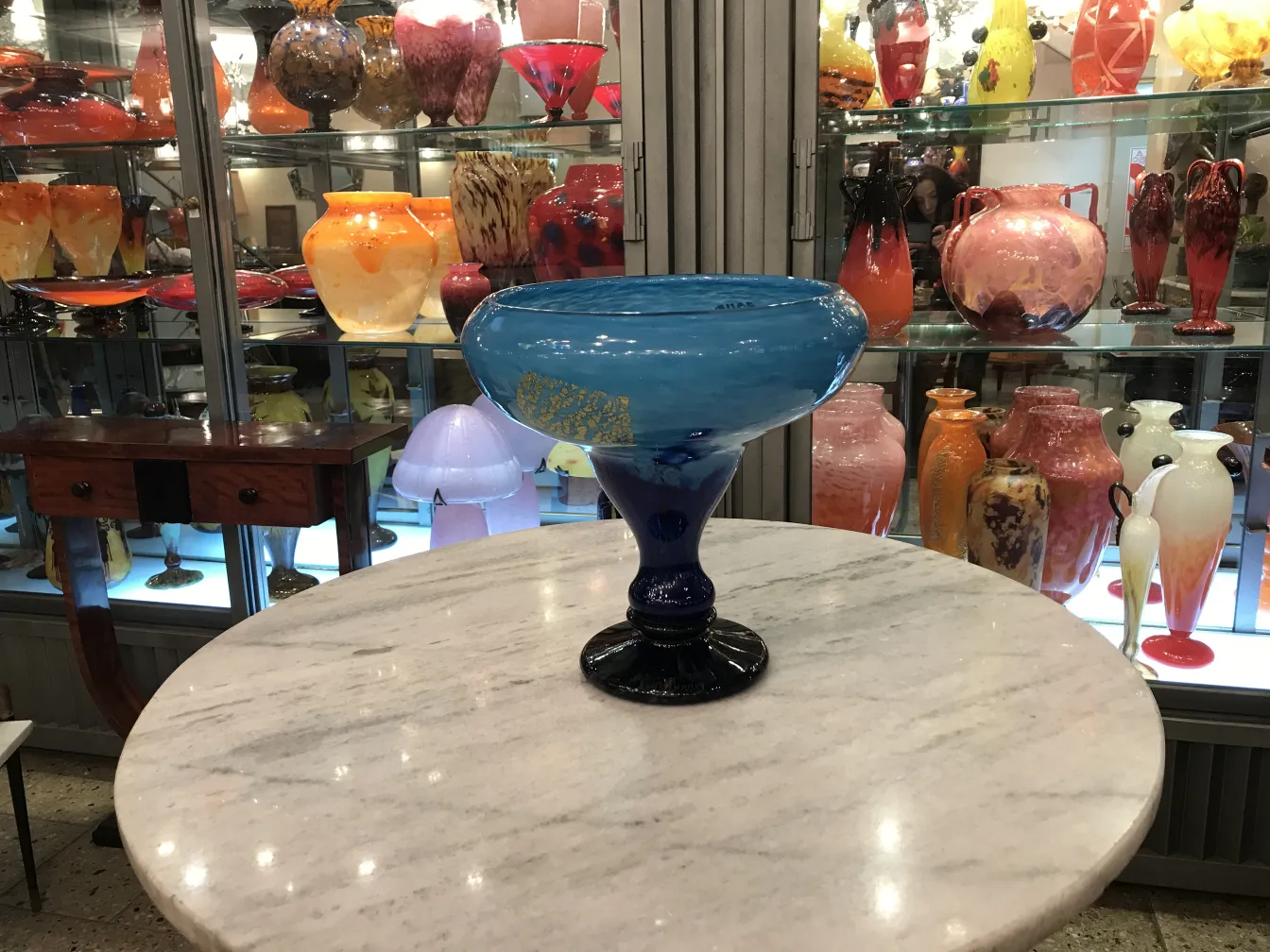 Vidrio firmado Daum Nancy de color azul sobre mesa de mármol con fondo de antigüedades.
