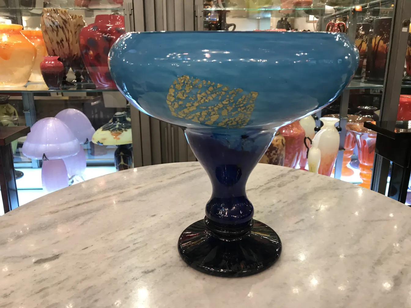 Vaso azul con firma visible, fondo negro y decoraciones doradas, rodeado de otros objetos antiguos.