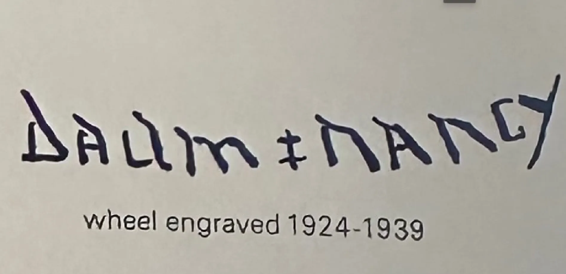 Vidrio firmado con letras Daum Nancy sobre fondo claro, ambiente antiguo.