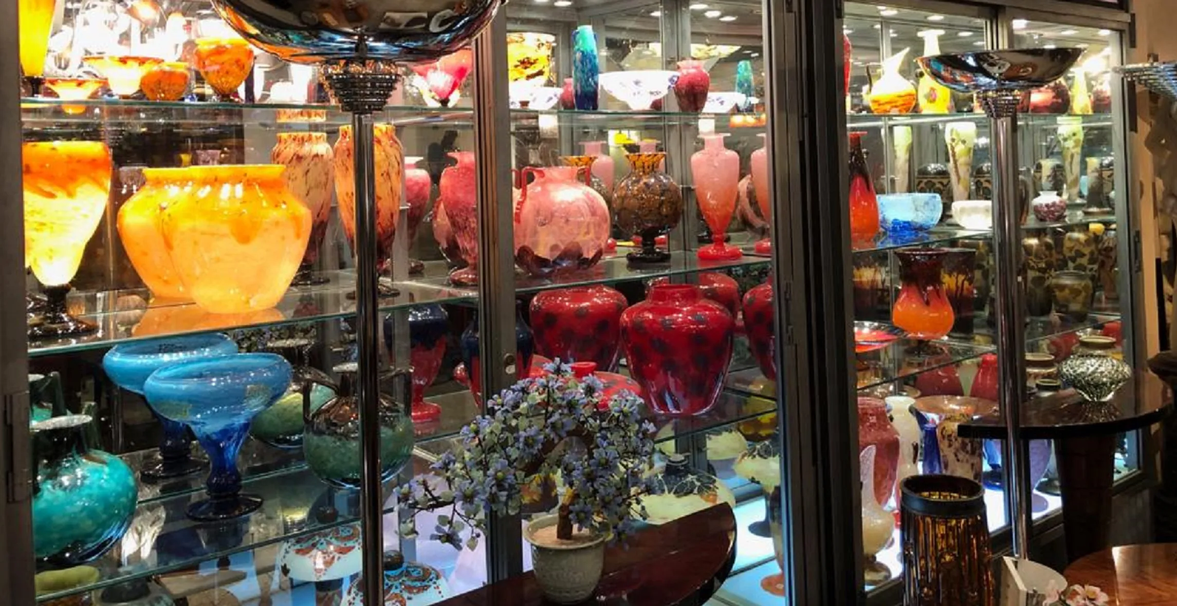 Collection d'antiquités avec verre signé Daum Nancy exposé dans une vitrine avec des couleurs vives