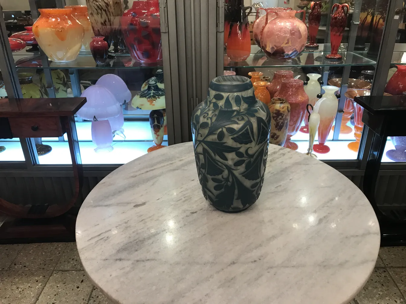 Antique signed glass Daum Nancy on a marble table with decorative objects in the background.