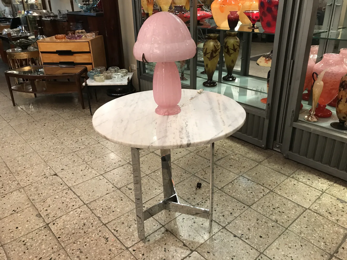 Vidrio firmado Daum Nancy sobre una mesa blanca con lámpara rosa en un ambiente de antigüedades.