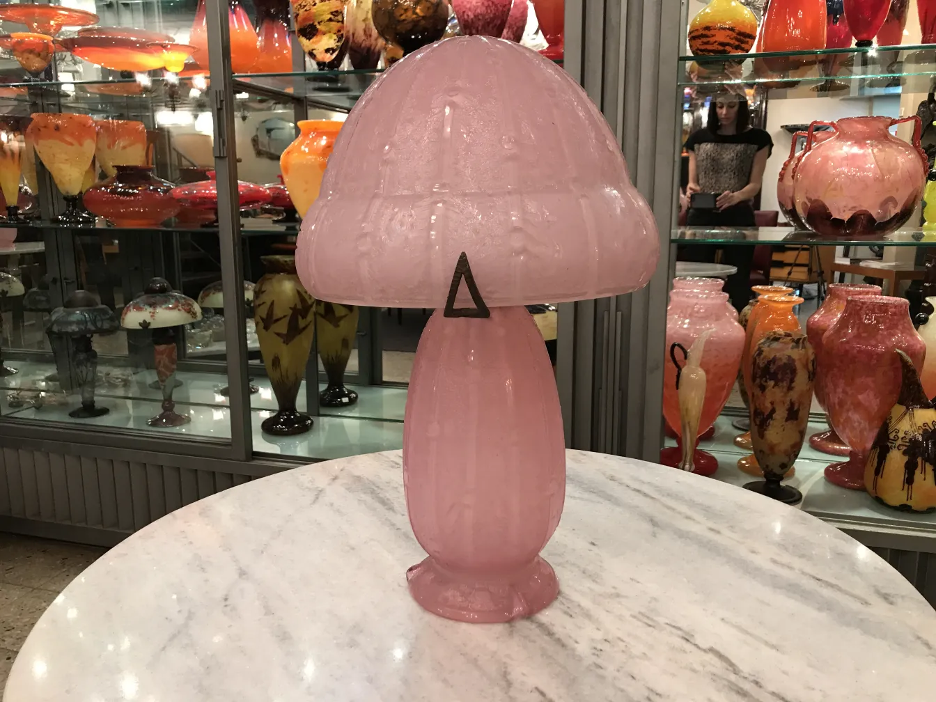 Pink glass lamp shaped like a mushroom with a background of various vases.