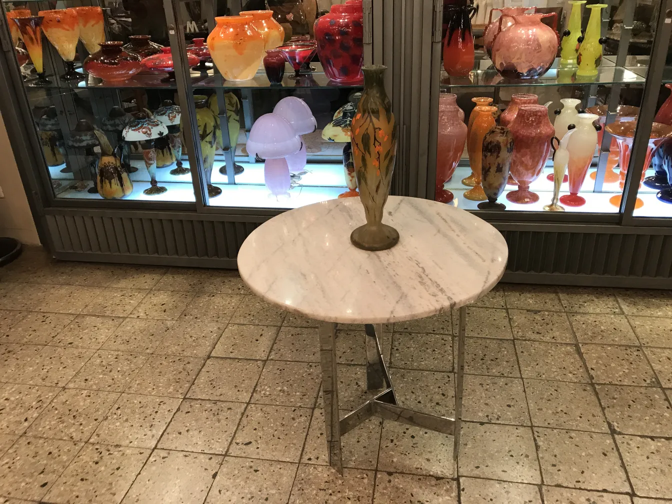 Vaso de vidro assinado Daum Nancy com decoração colorida, cercado por outras antiguidades.