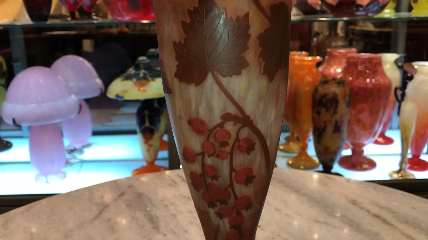 verre signé Daum Nancy avec motif de feuilles et fleurs sur fond clair, entouré d'autres objets anciens