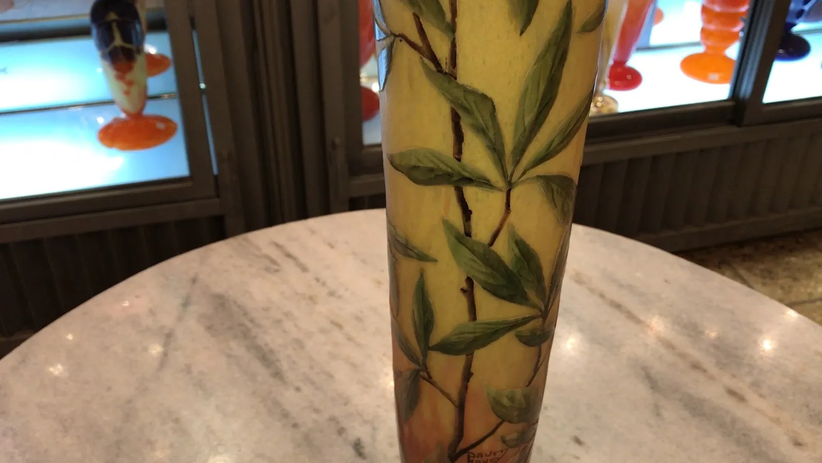 Signed glass with green leaves on yellow background in an antique setting.