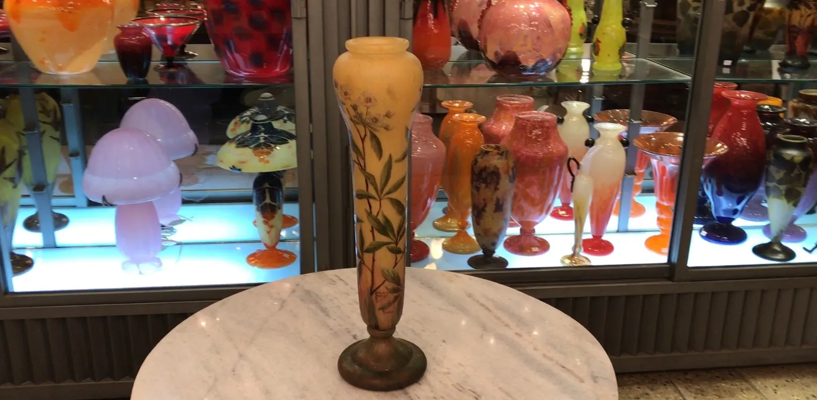 Vidrio firmado Daum Nancy con florales y colores suaves en un entorno de antigüedades.