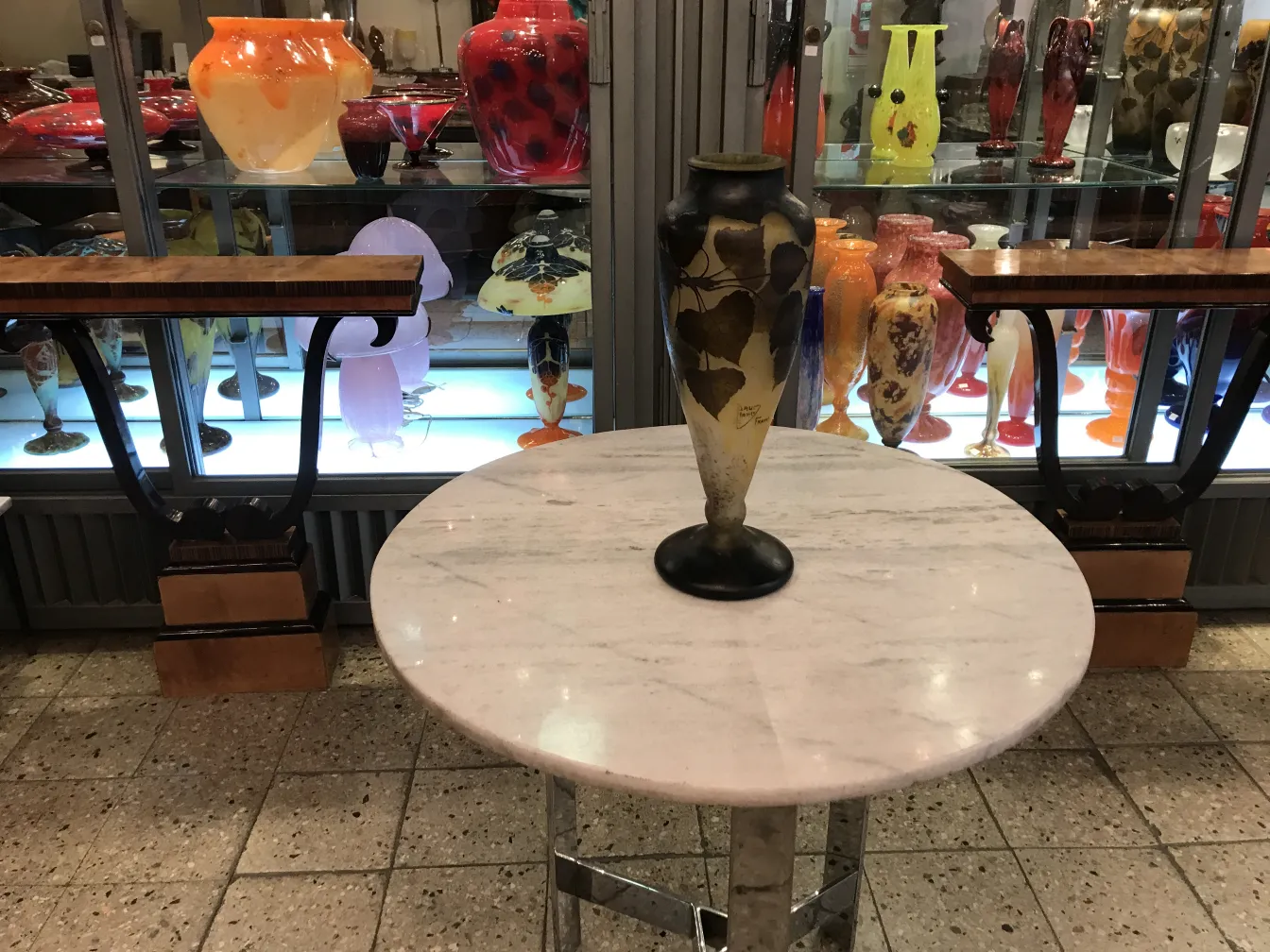 Dekorative Vase aus signiertem Glas Daum Nancy mit Blättern, beleuchtet von anderen bunten Glasobjekten.