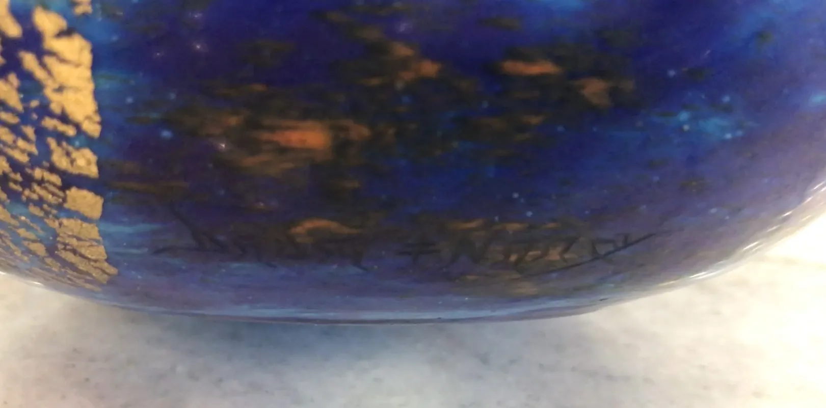 Vidrio azul firmado Daum Nancy con detalles dorados en un fondo claro.