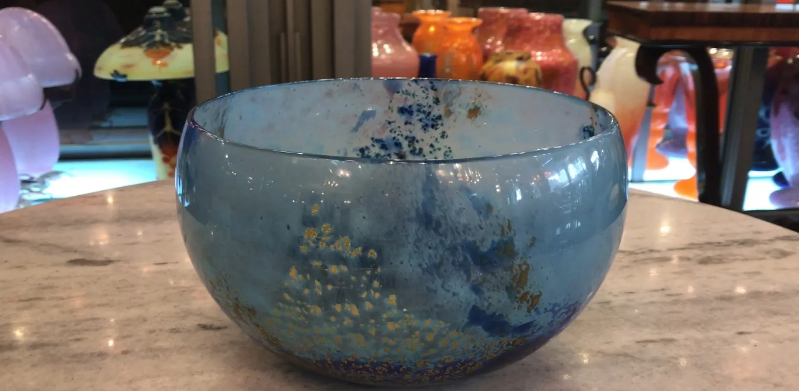 Vidro decorativo assinado Daum Nancy em tons de azul e dourado contra fundo branco.