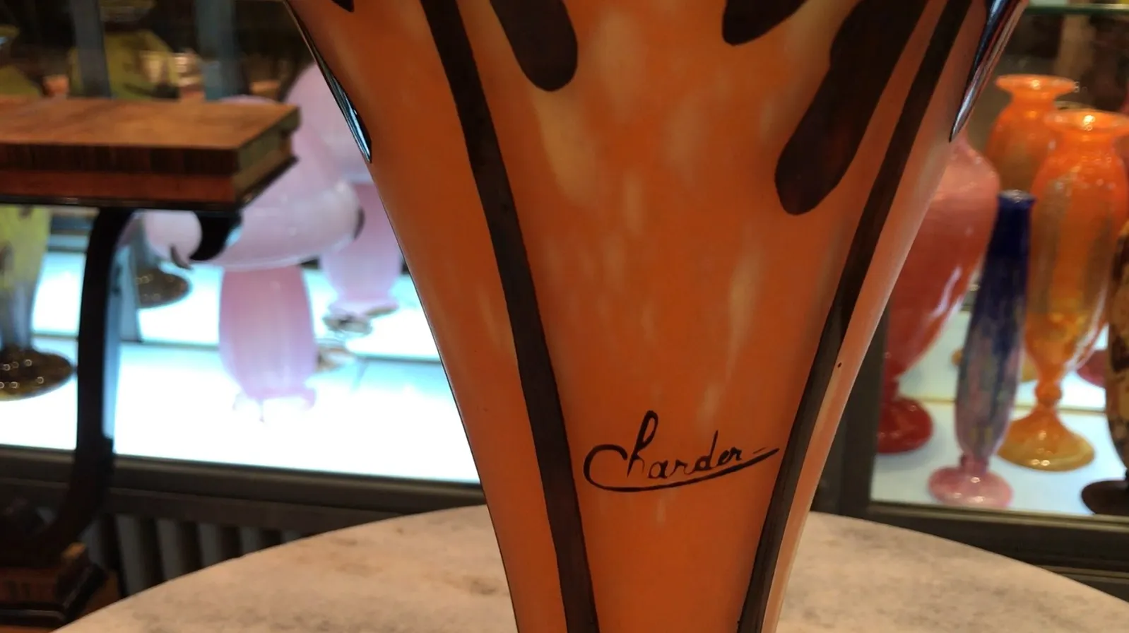 Vidrio antiguo firmado por Charder con tonos naranja y detalles decorativos, en un entorno de antigüedades.