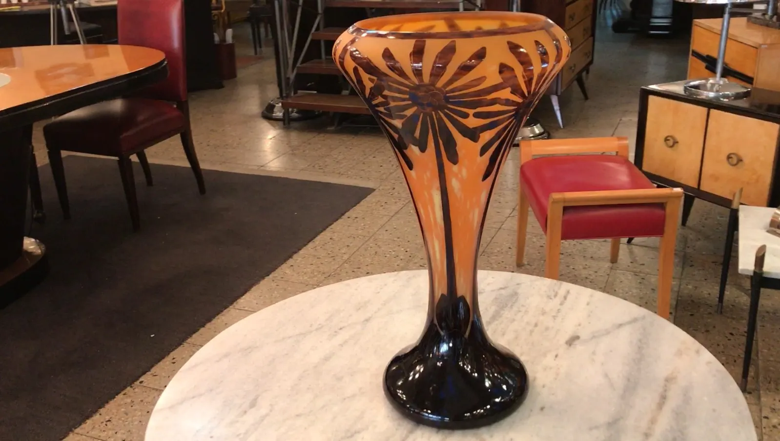 Antigua obra de vidrio firmado Charder con diseño de flores, fondo anaranjado. Contexto moderno.