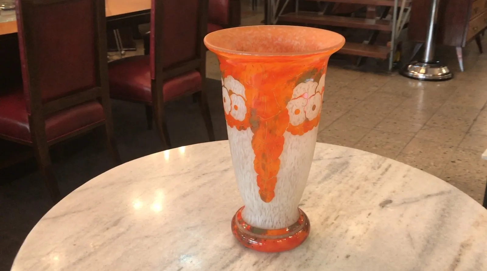 Vaso de vidrio firmado Charder con diseños florales en tonos naranjas y blancos. Ambiente cálido