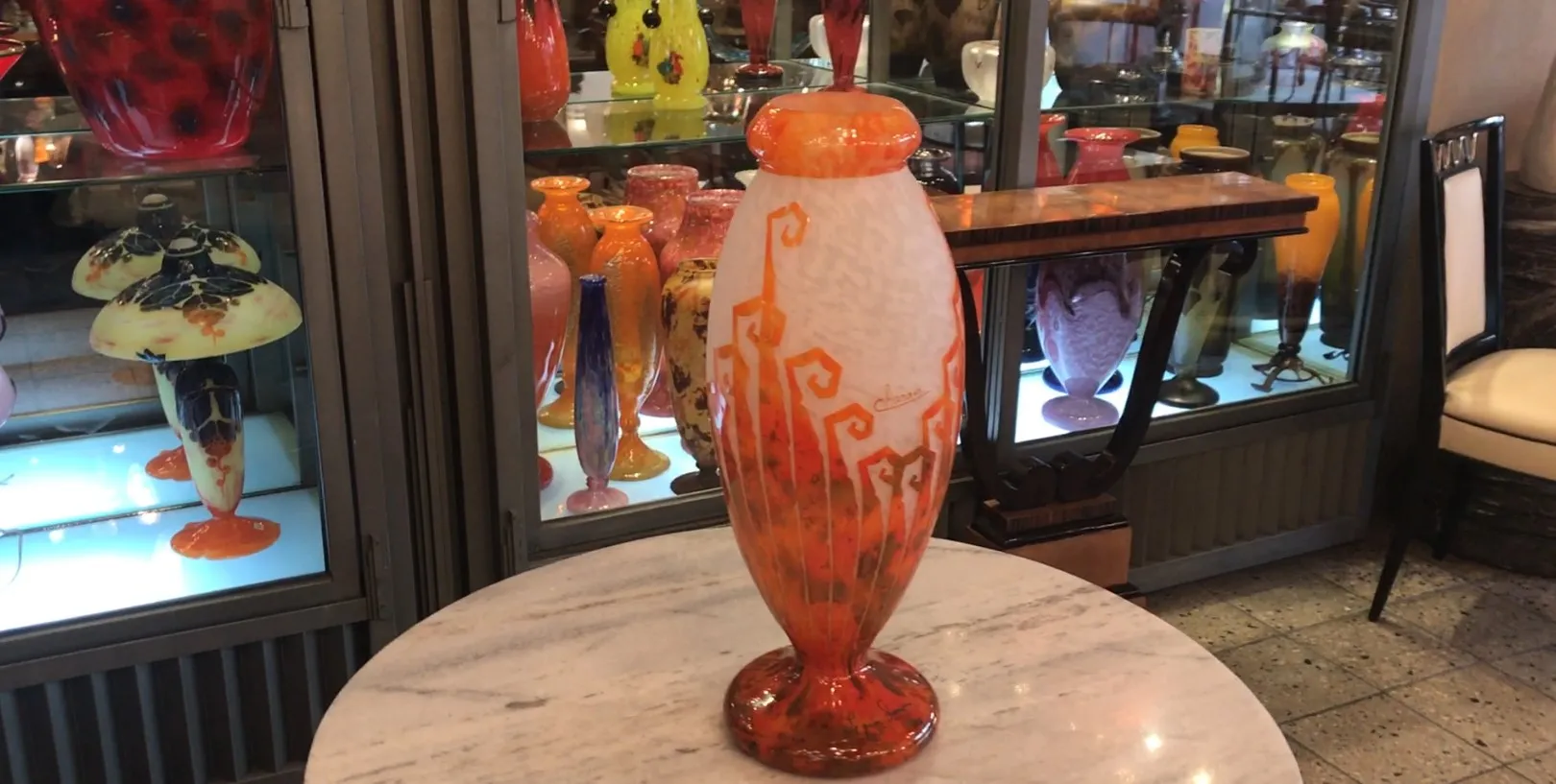 Vidrio firmado Charder con diseño vibrante en tonos cálidos, exhibido entre otros objetos de antigüedades.