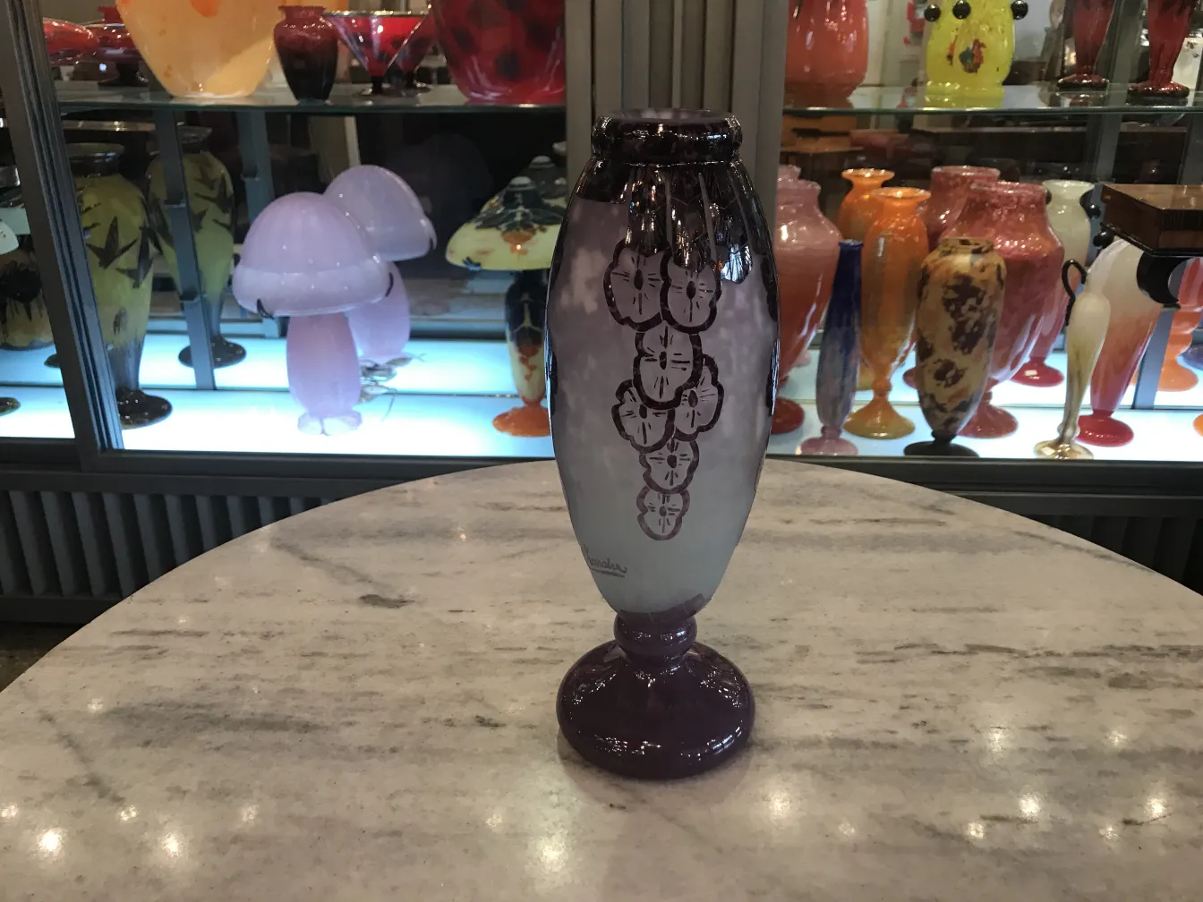 Side view of signed glass Charder featuring purple and light designs, surrounded by colorful antiques.