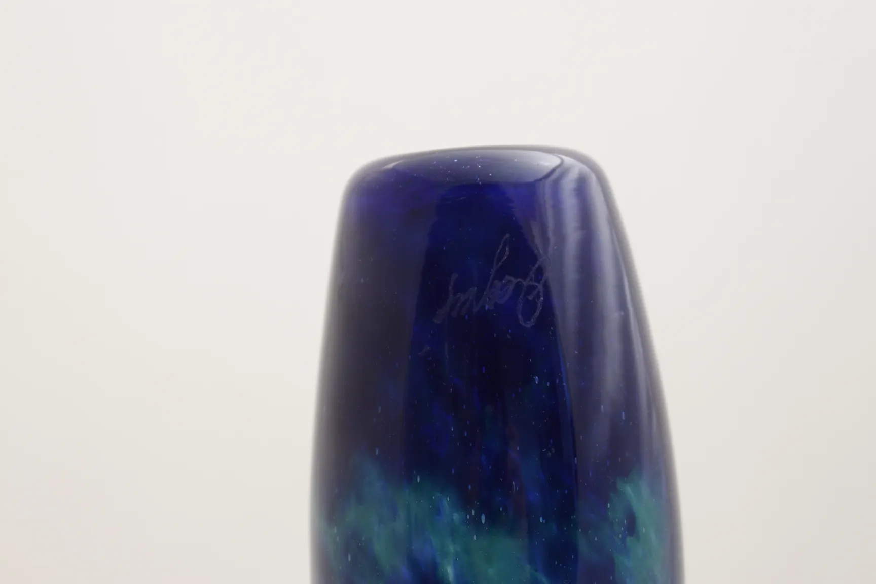 Vidrio antiguo firmado Degué con colores azul y verde en un fondo simple.