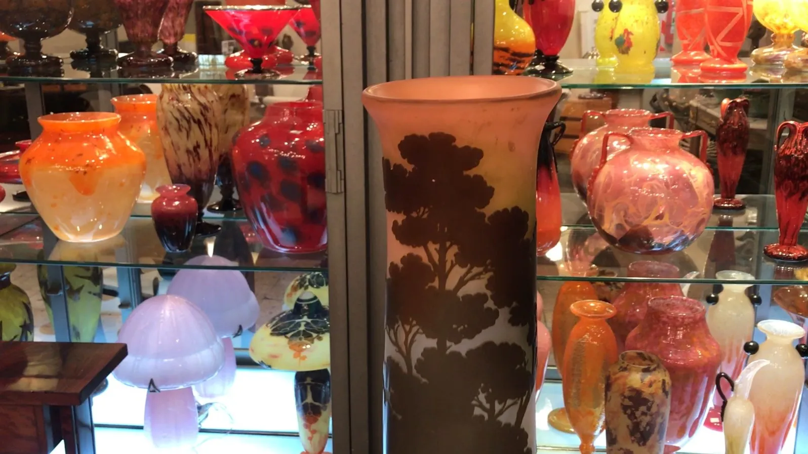 Vaso antigo com design de árvores, exibido com itens de vidro coloridos