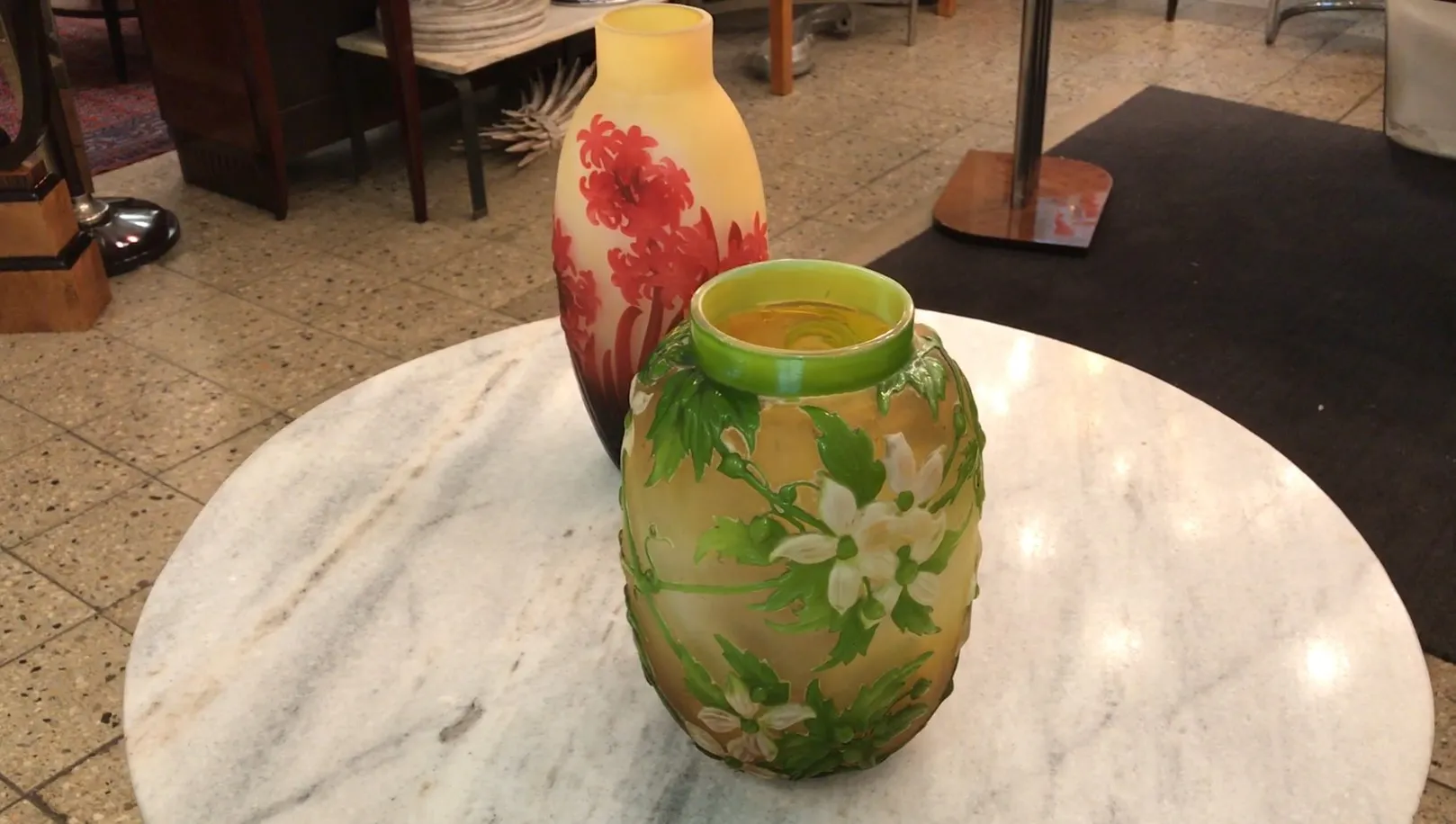 Two antique vases of signed glass Gallé with floral designs on a marble table.