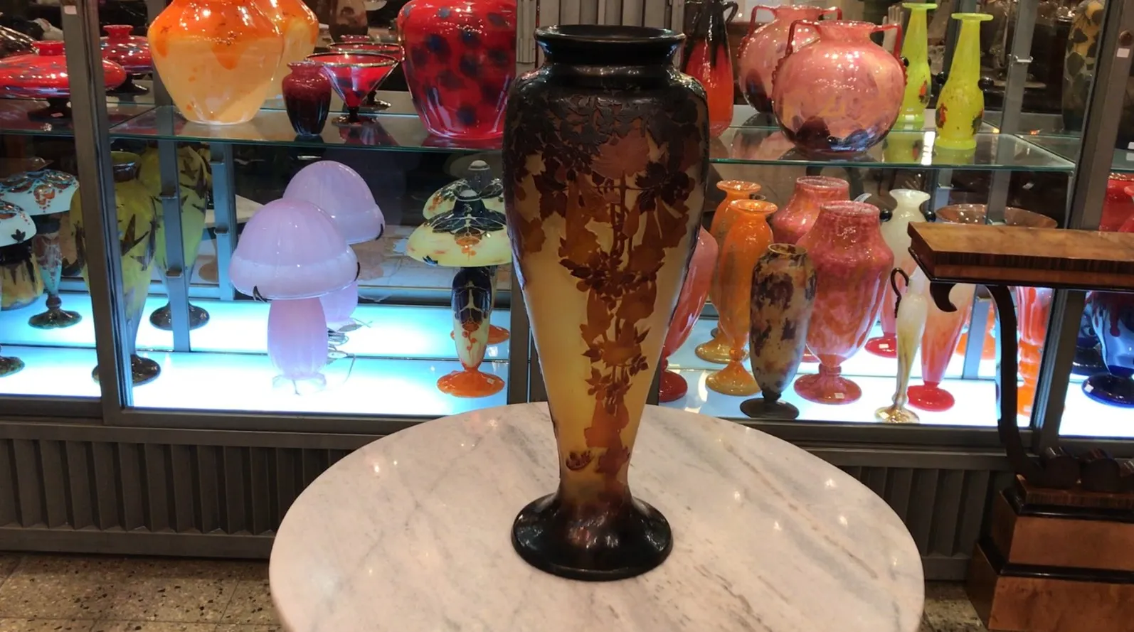 Vaso antigo assinado Gallé com detalhes florais, exposto em uma vitrine.
