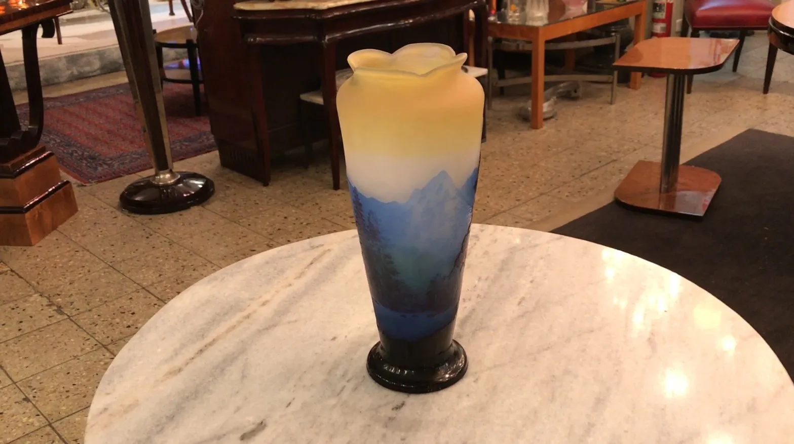 vidro assinado antigo gallé, com características artísticas, decorado em tons de azul e amarelo, sobre uma mesa de mármore