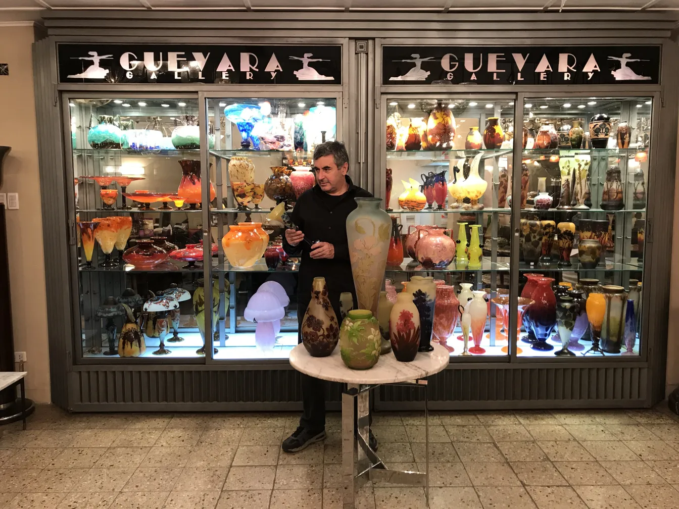 古董签名玻璃Gallé在展览柜中，旁边有其他色彩丰富的装饰物品。