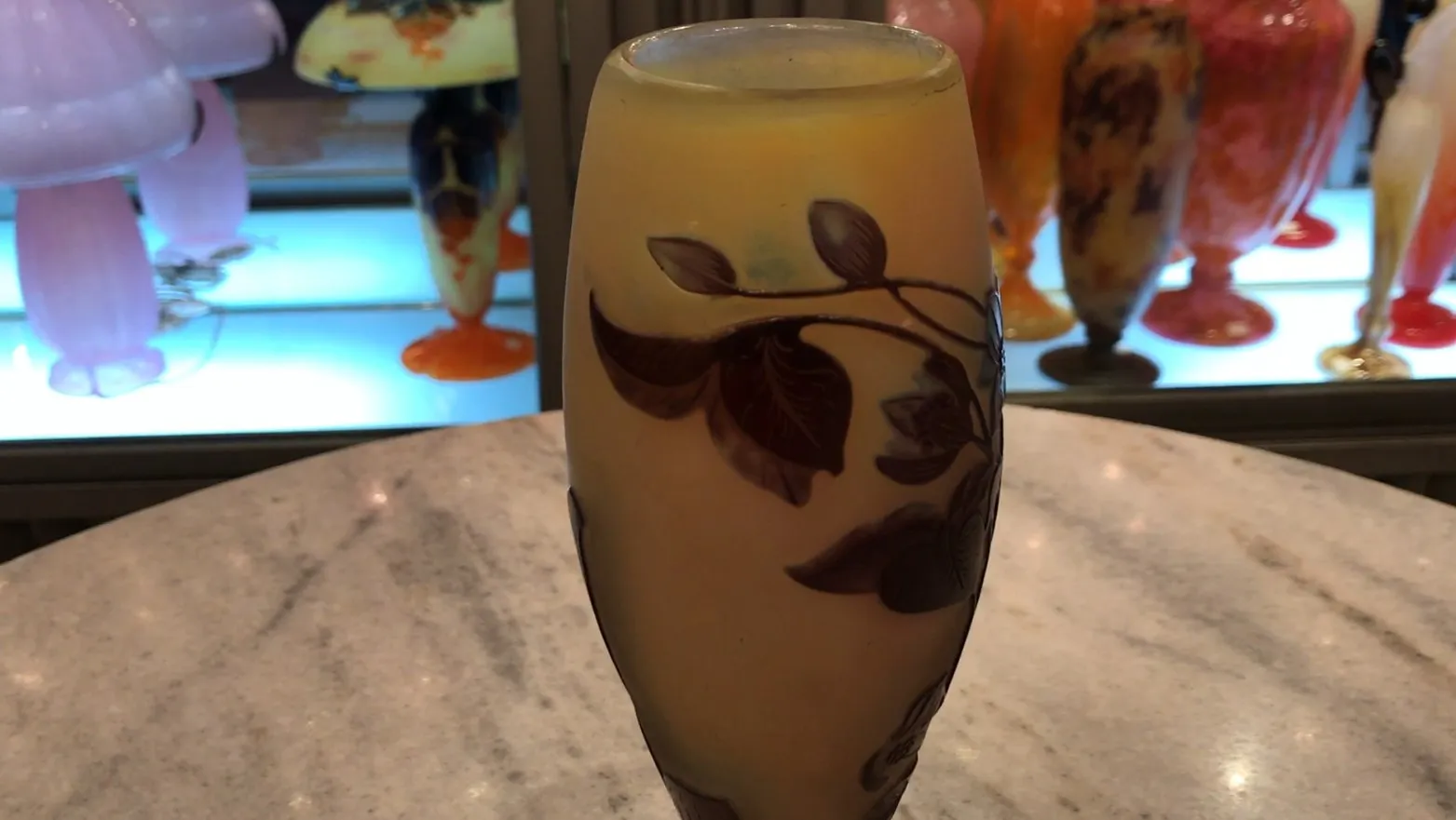 Vase mit Blätterdesign in Gelb und Braun, Hintergrund mit anderen antiken Objekten.