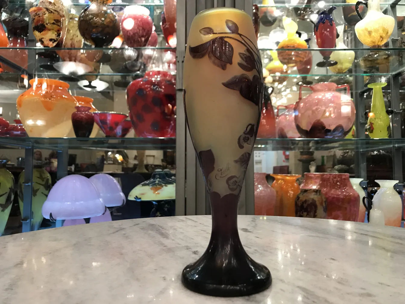 Vetro firmato Gallé con design floreale su sfondo chiaro, circondato da varie antichità.