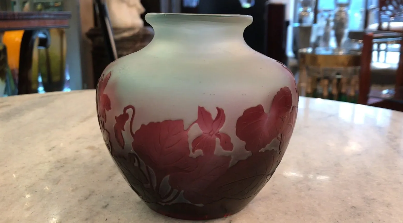 Ancien verre signé Gallé avec décoration florale en tons rouges et verts, sur une table en marbre.