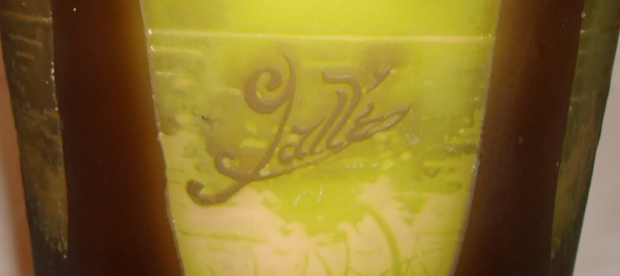 Signiertes Glas Gallé mit dekorativen grünen und gelben Details, ein antikes Stück in einem eleganten Ambiente.