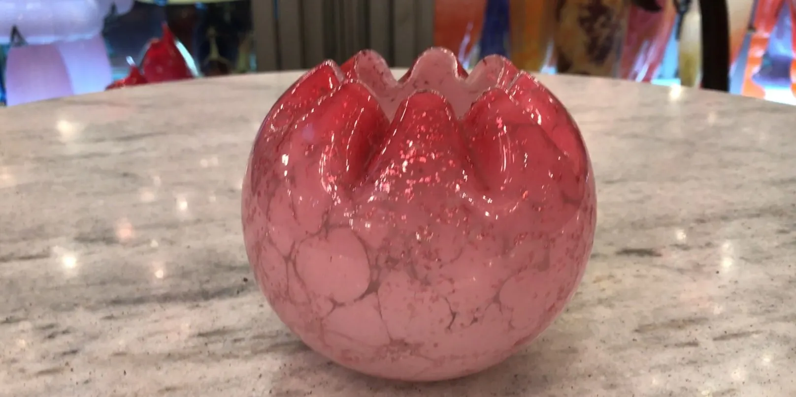 Vidro com assinatura em tons de vermelho, decoração antiga em mesa de mármore.