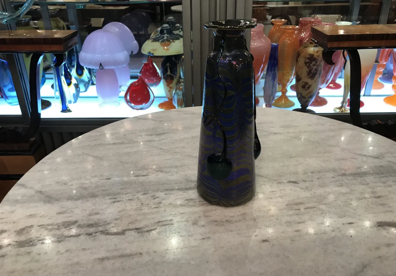 Vecchia bottiglia in vetro firmato Loetz con motivo blu e nero su un tavolo in marmo.