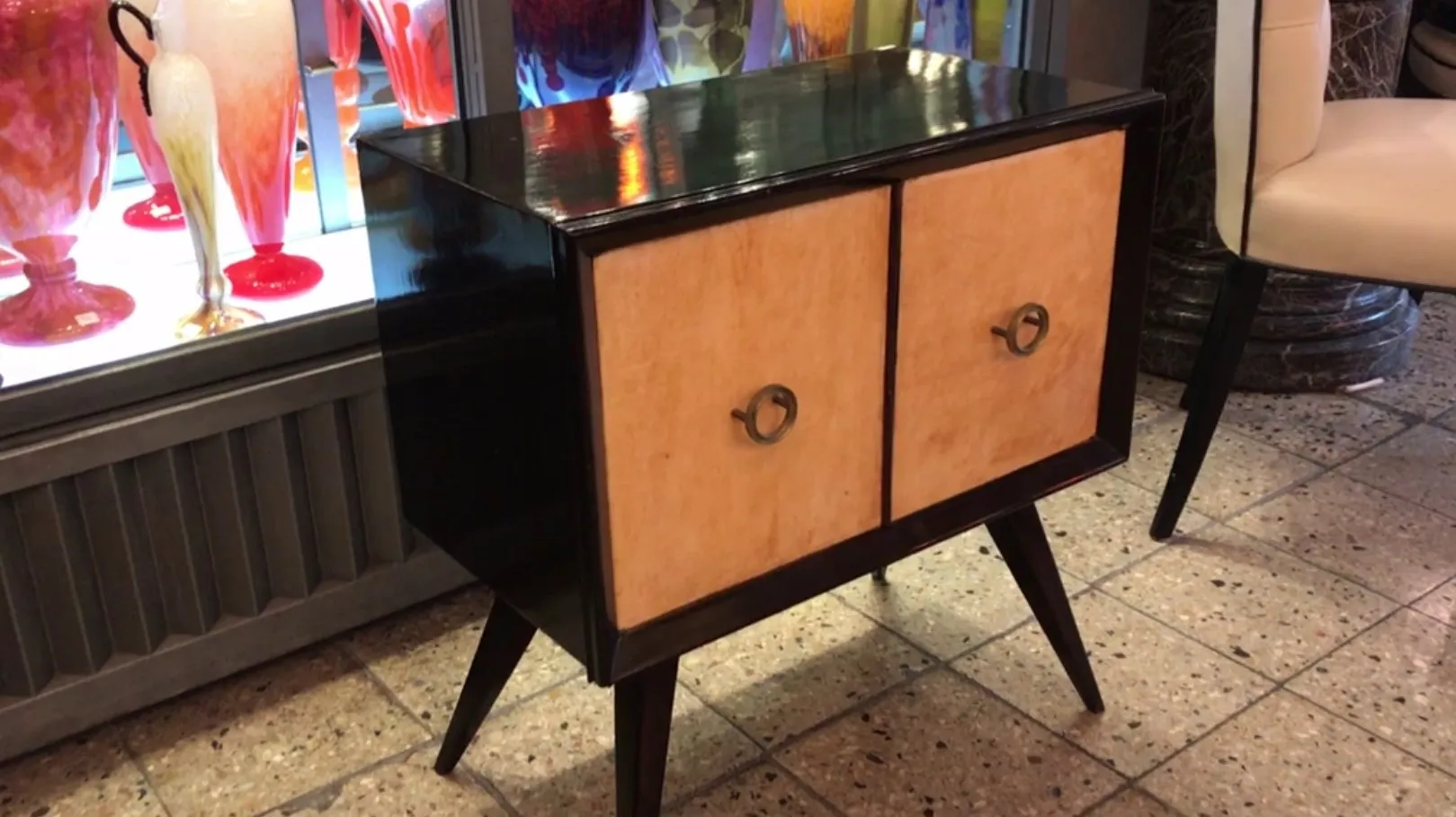 mesa de luz antiga com acabamento brilhante e portas em madeira clara, ambientada de maneira elegante