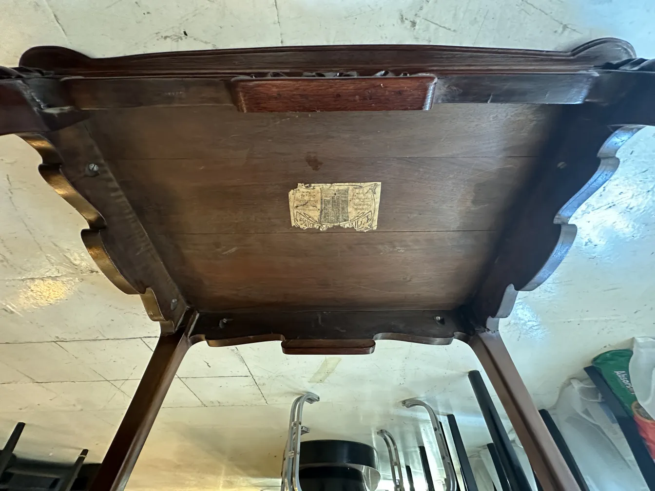 Visão inferior de uma mesinha antiga com detalhes decorativos.