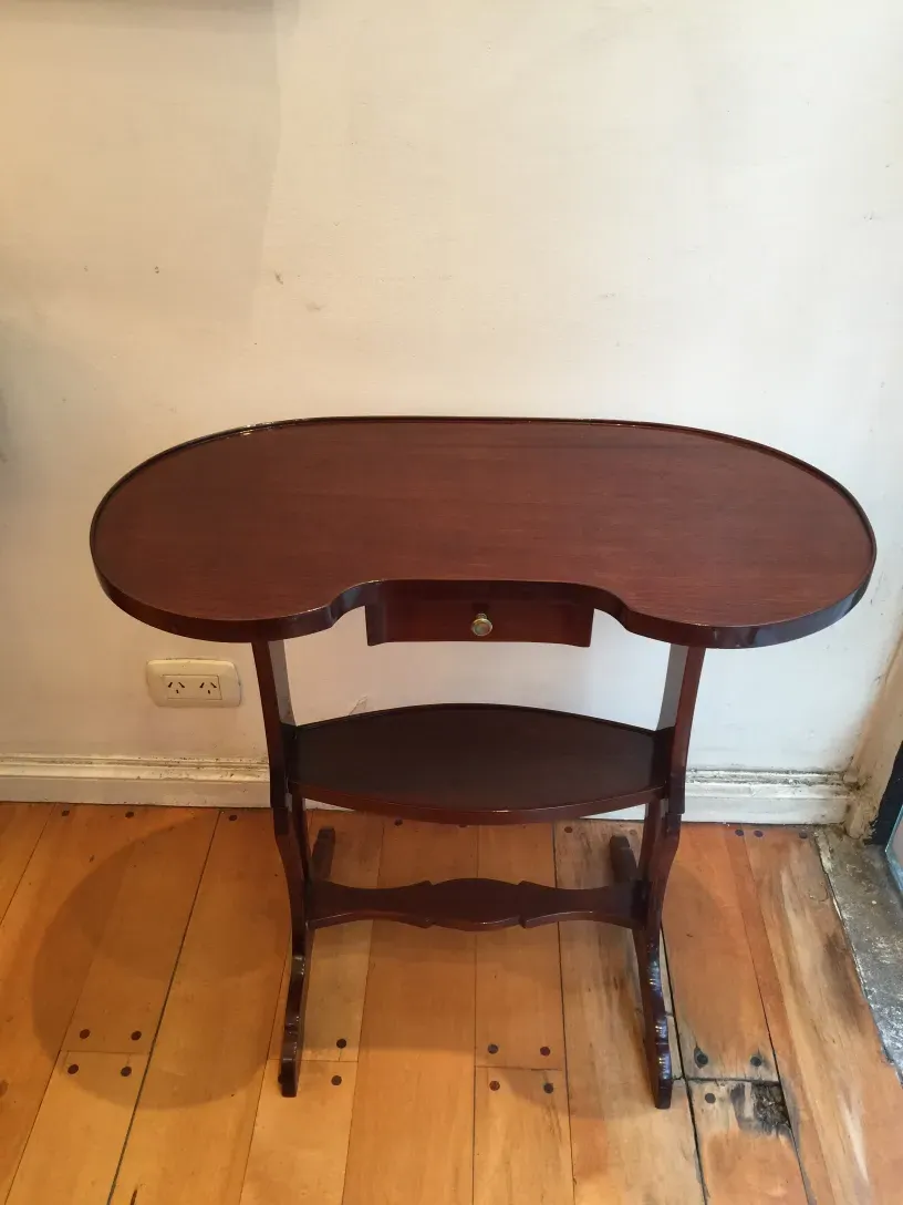 Tavolino antico con piano ovale e gambe decorative, sfondo neutro.