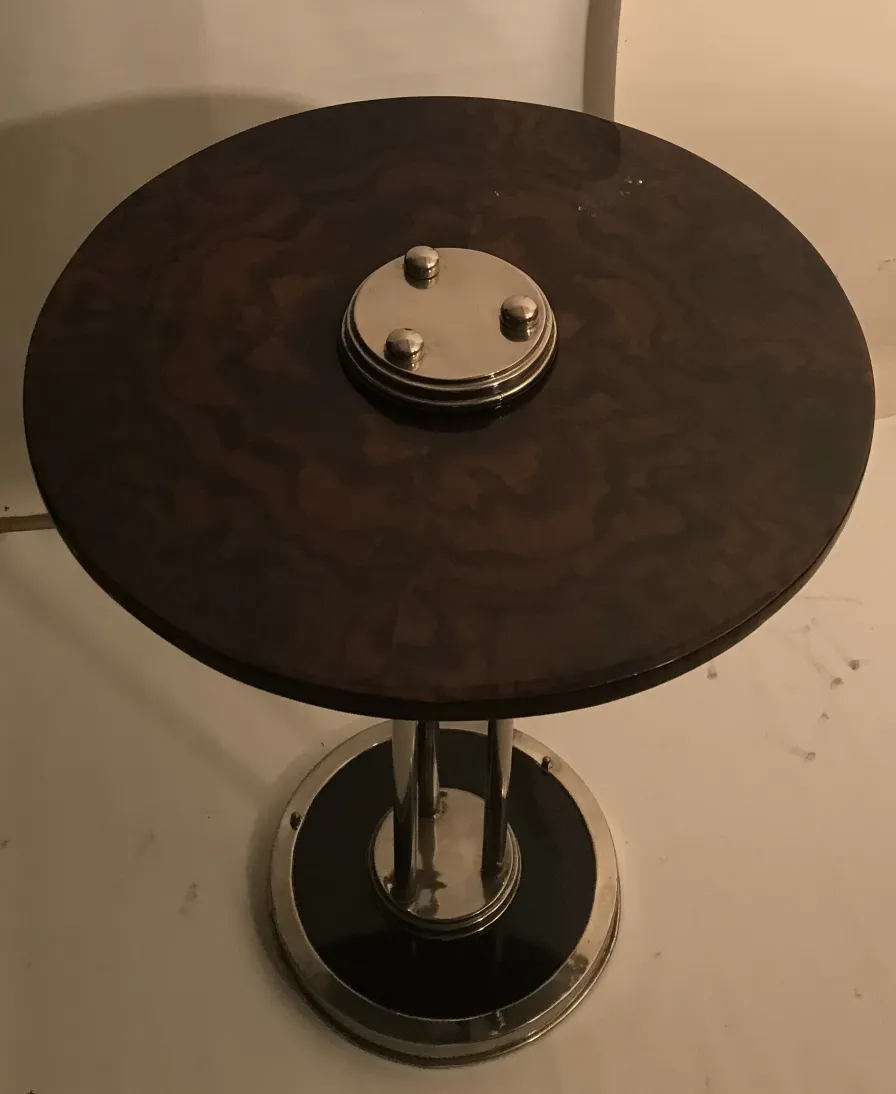Petite table ronde ancienne avec des détails métalliques brillants, sur fond clair.