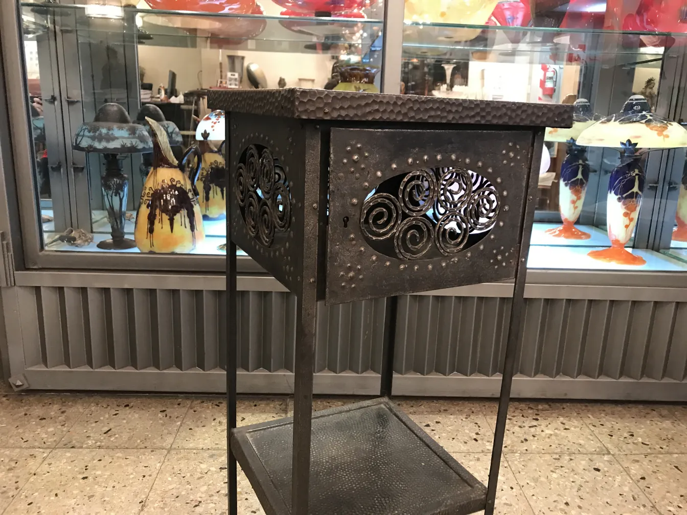 Petite table ancienne décorative avec un design incurvé, placée dans un environnement classique avec divers objets de collection.