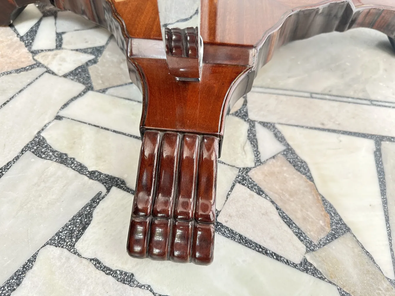 detalle de la pata de una mesita antigua sobre un piso de piedra.