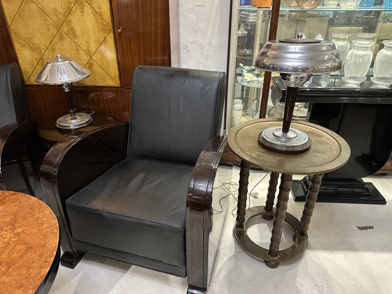 Petite table antique ronde à côté d'un fauteuil noir et d'une lampe.