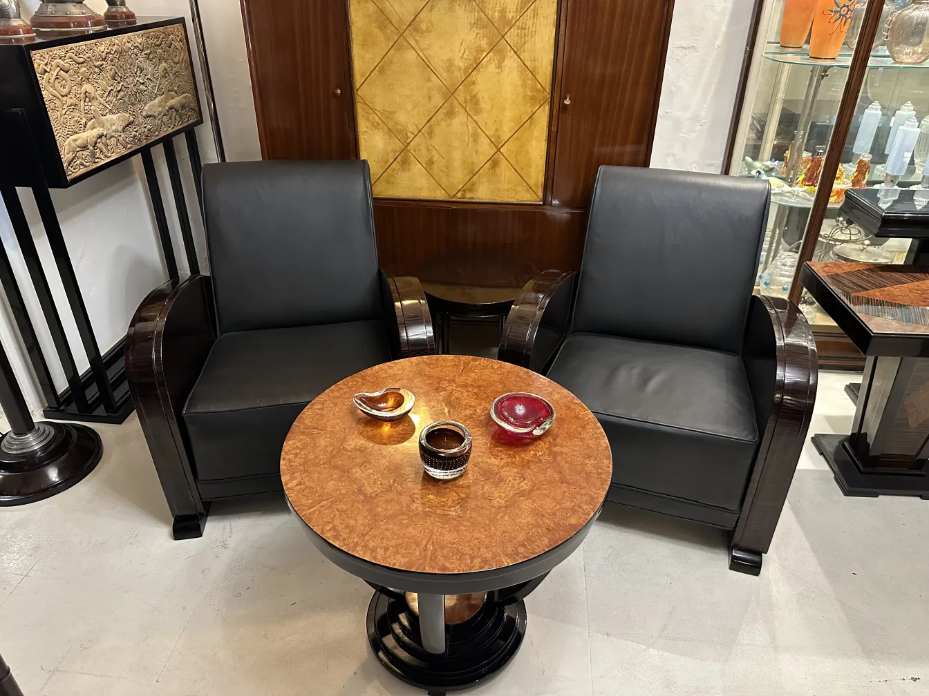 Tavolino antico con superficie decorativa, circondato da poltrone in pelle nera in un ambiente accogliente.